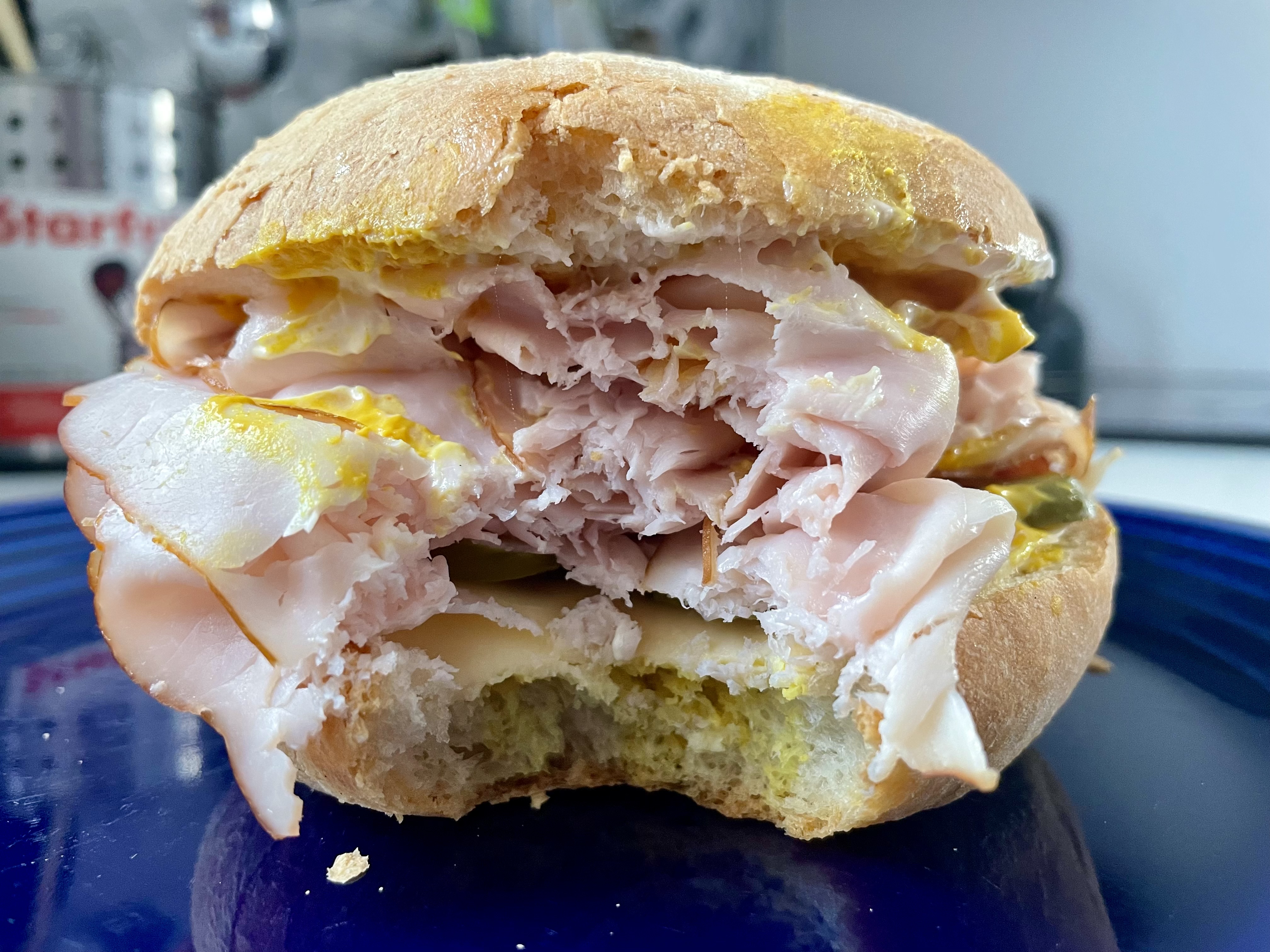 A hearty turkey sandwich on a freshly baked kaiser roll, piled high with flavourful deli meats, tangy pickles, and just the right amount of mayo and mustard