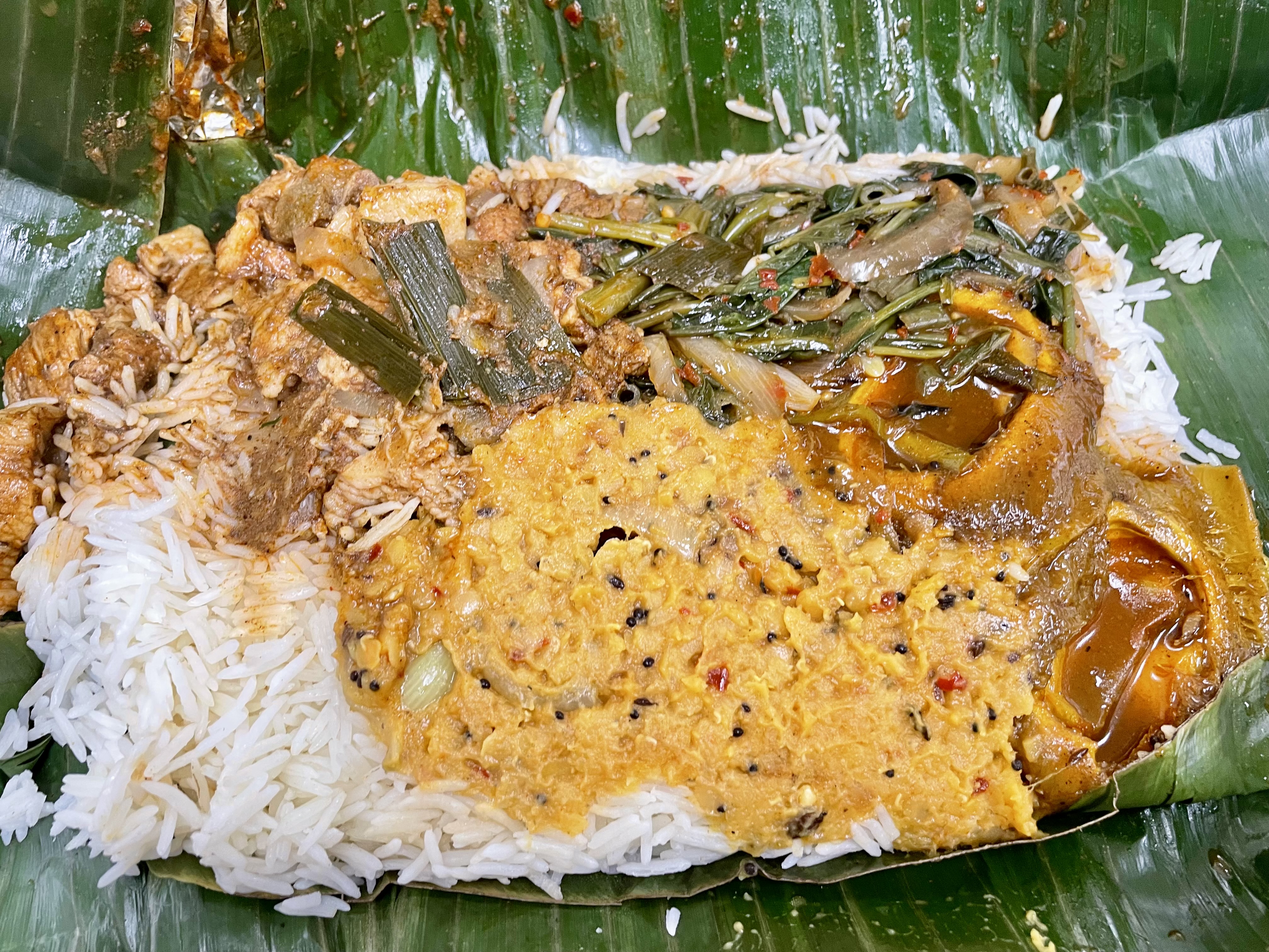 A fiery spread of black pork curry, mustardy lentils, curried greens, tart mango, and crisp poppadum—all served on a traditional banana leaf that’s as much about flavour as it is about feeling right at home.