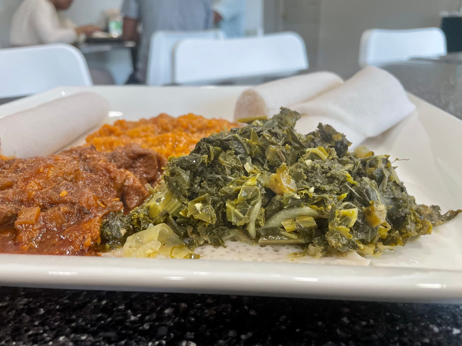 A vibrant trio of chicken stew, spiced lentils, and tender kale, all nestled on pillowy enjera—comfort food crafted with heart, heat, and home